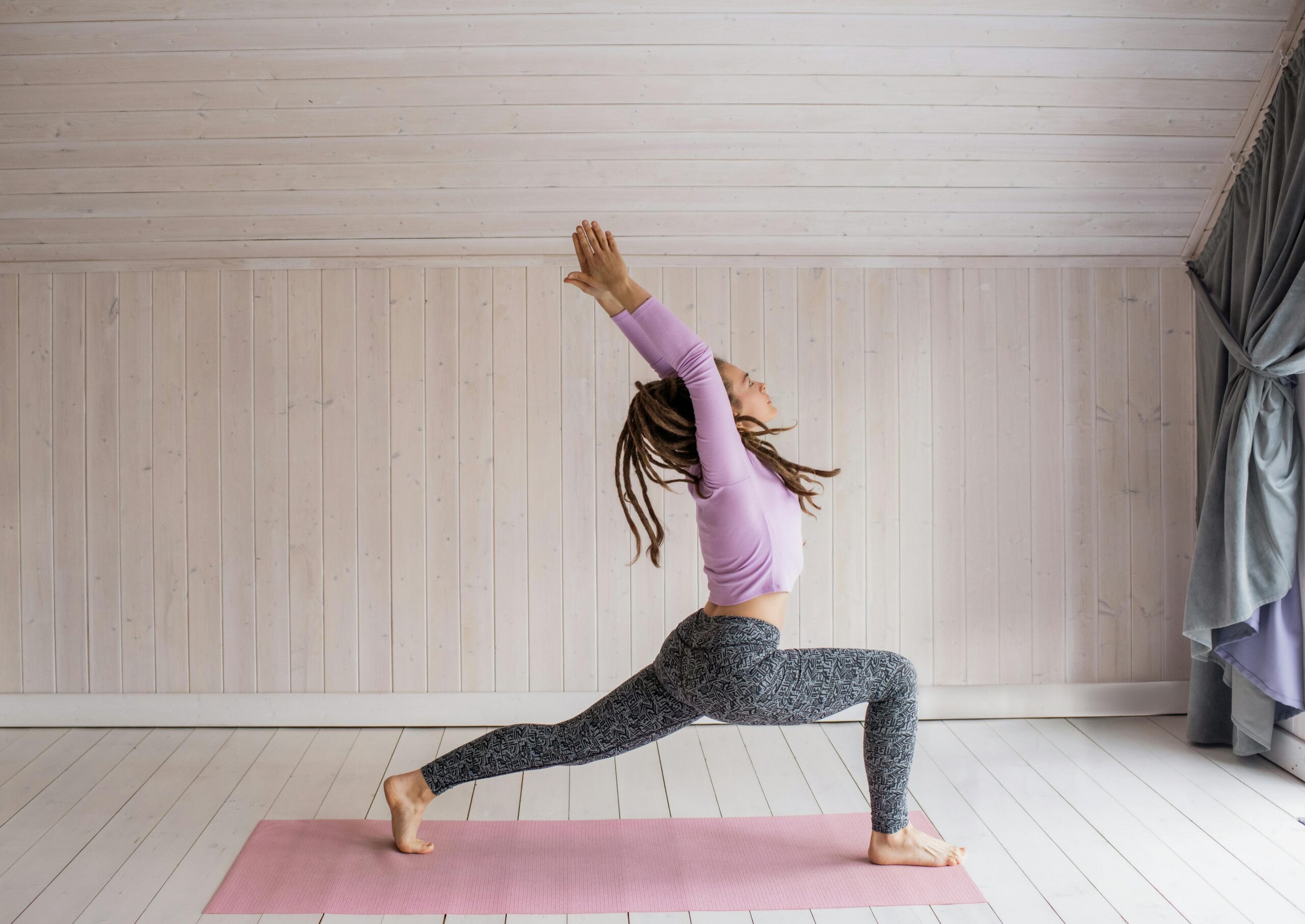 A woman in activewear performs a yoga pose on a pink mat indoors, promoting wellness and fitness.