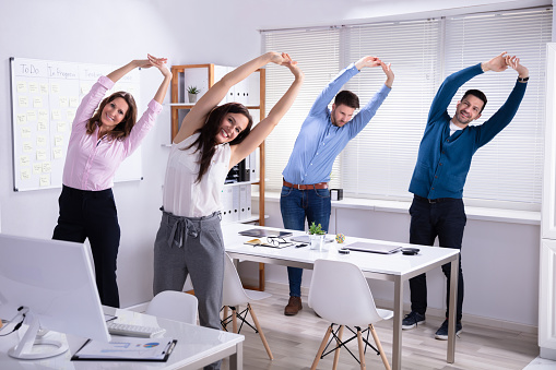 happy businesspeople doing stretching exercise behind desk at workplace